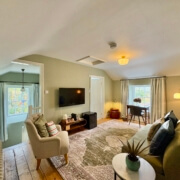 A cozy, light-filled living room at this Bed & Breakfast in Penzance features a green sofa, armchair, TV, and a small desk by the window. Wooden floors and neutral walls create a warm, inviting atmosphere for your stay. Sancreed House Retreat